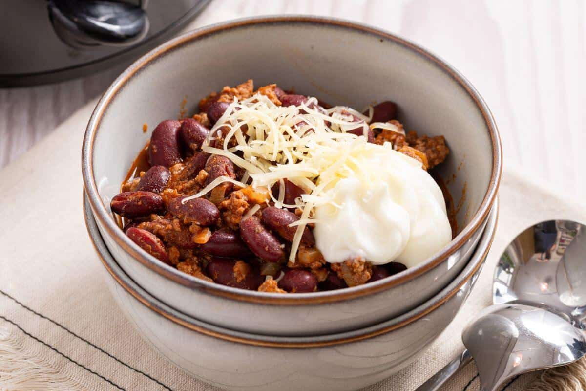 A bowl of chili for two with cheese and sour cream.