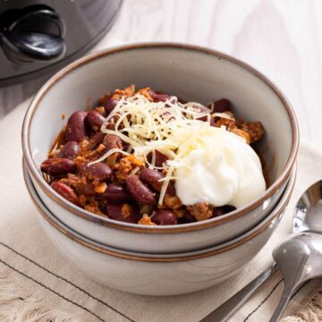 A bowl of chili and sour cream in front of a slow cooker, perfect for two.