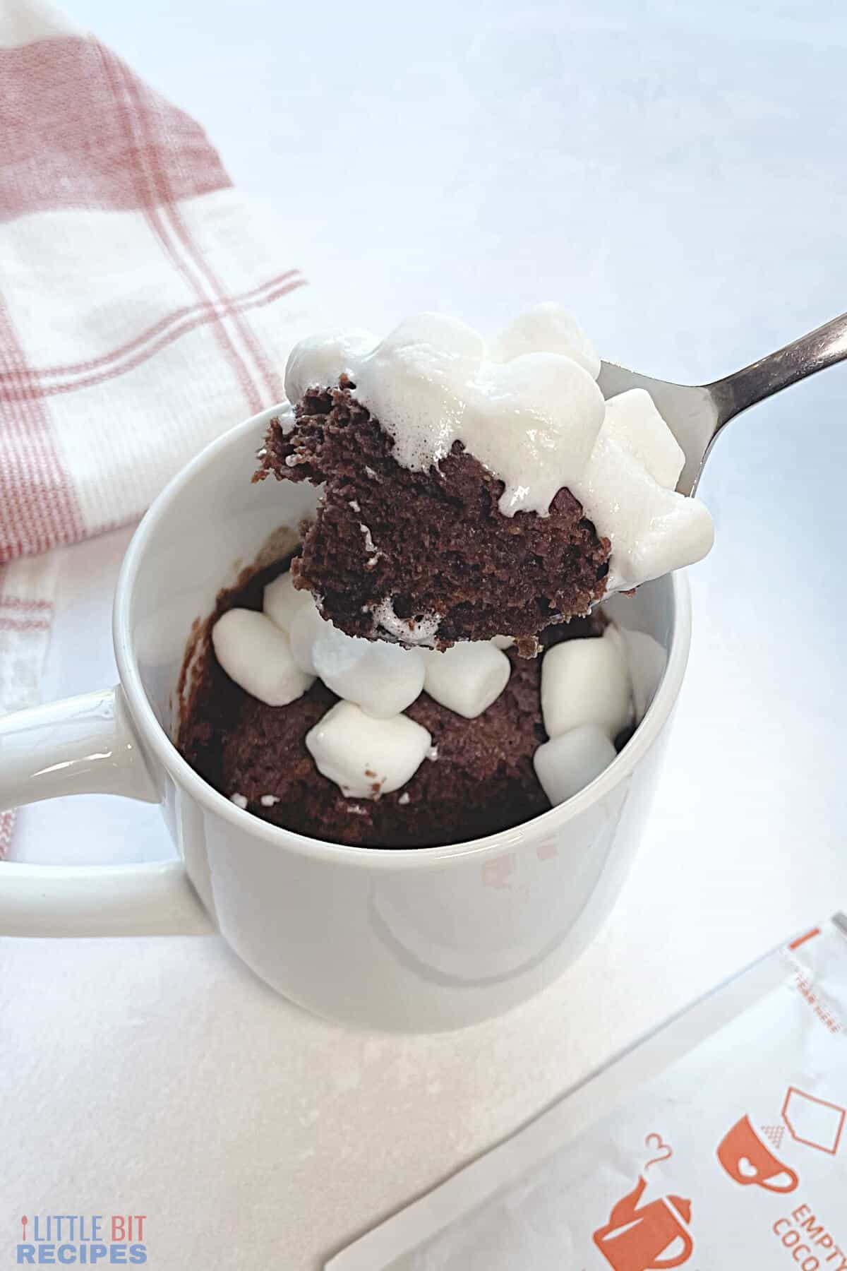 hot cocoa mug cake topped with marshmallow showing spoonful.