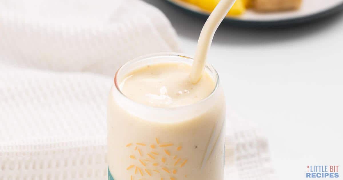 Pineapple banana smoothie in glass with straw.