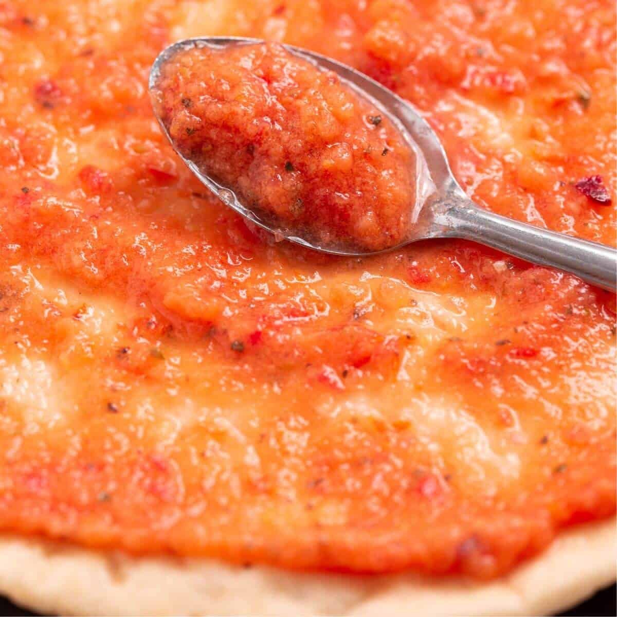 sauce on spoon spreading onto pizza crust.