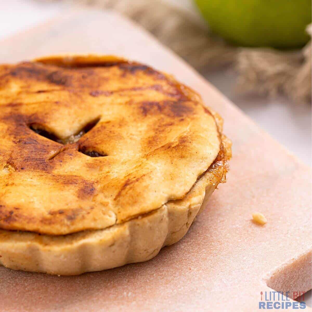 single serve pie on cutting board with apple in back.