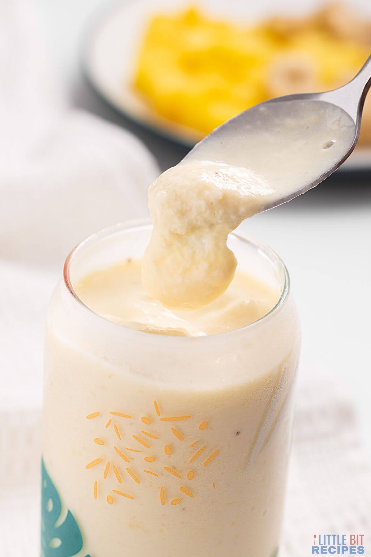 pineapple banana smoothie pouring from spoon over glass.