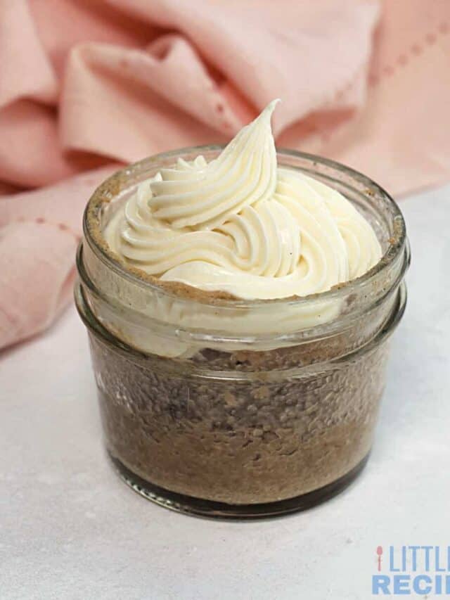 A glass jar filled with chia pudding topped with a swirl of cream, set against a pale pink cloth background.