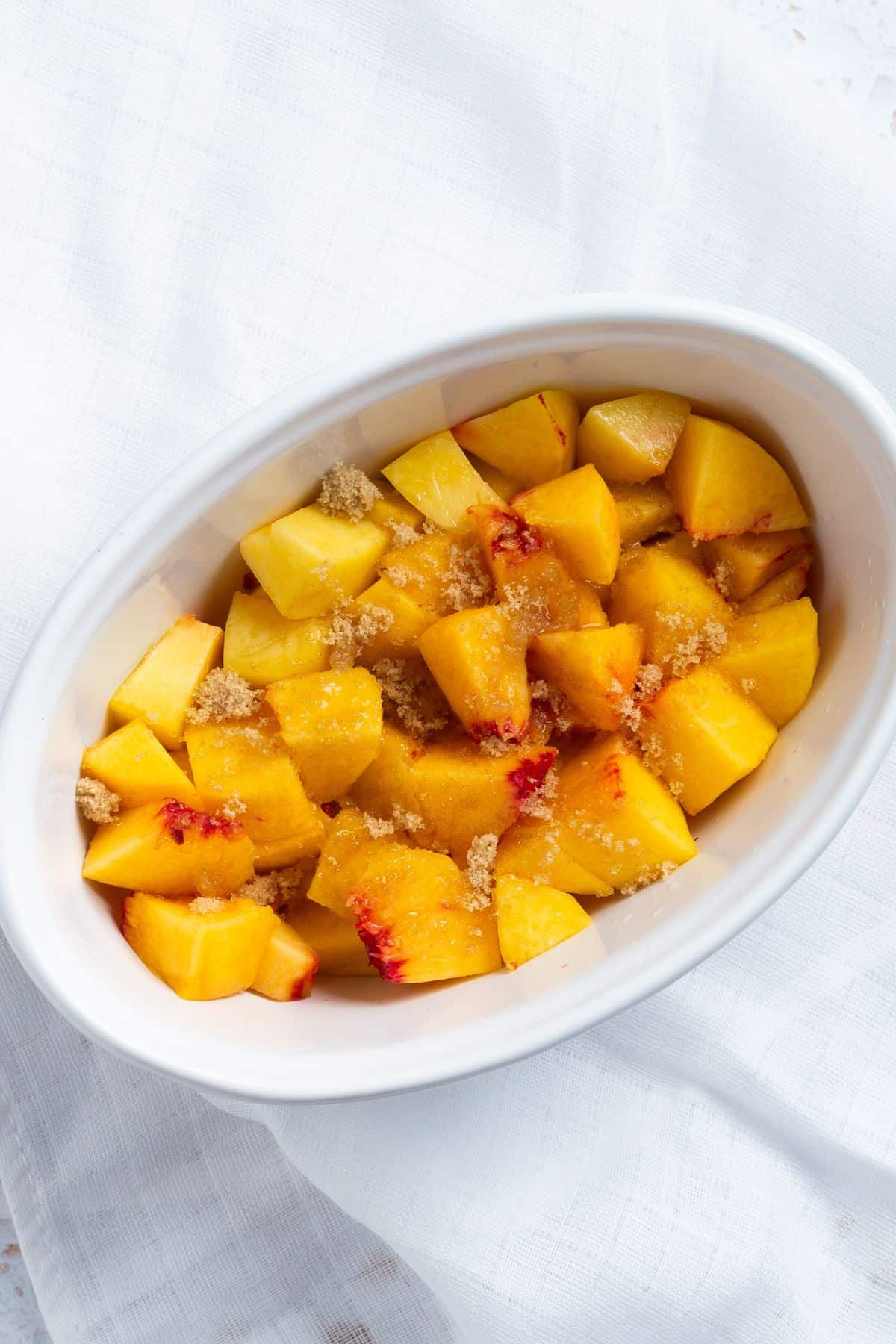 Sliced peaches in a small white baking dish for a peach cobbler for one.