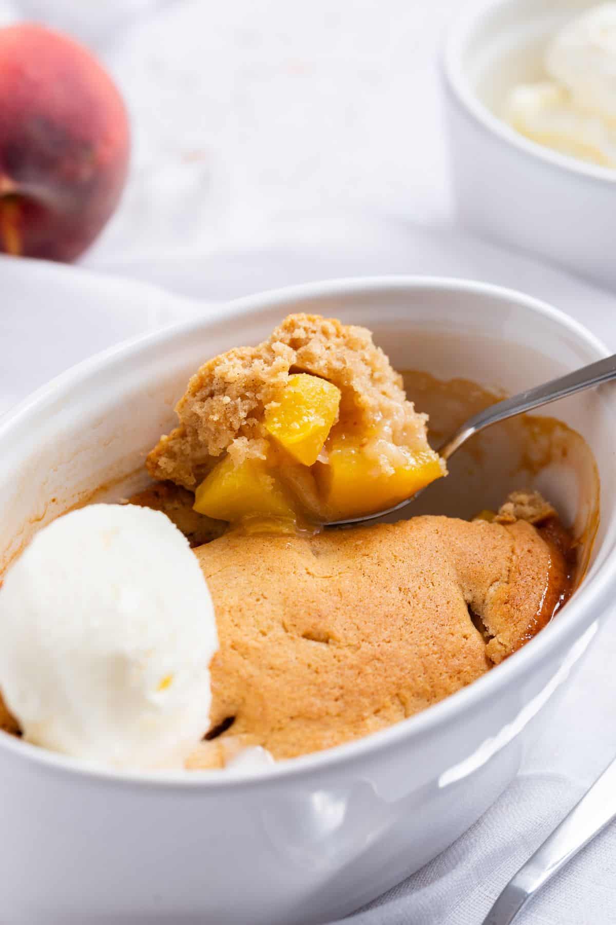 Peach cobbler for one served with ice cream and peaches.