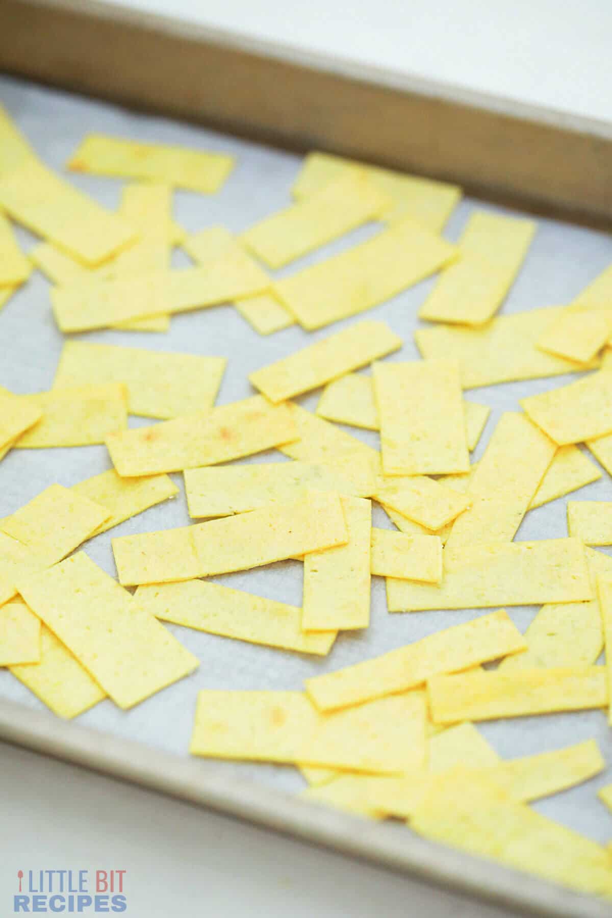 unbaked tortilla strips on parchment paper lined sheet pan.