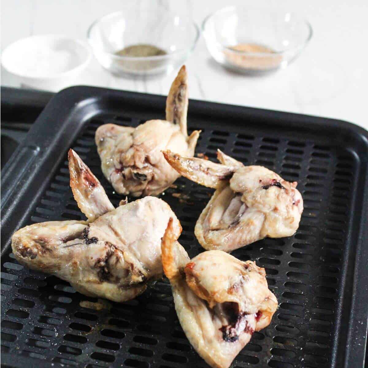 partially cooked seasoned chicken wings on air fryer tray.