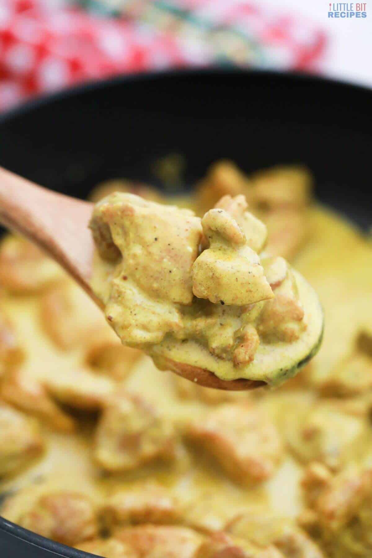 wooden spoon with chicken curry over skillet.