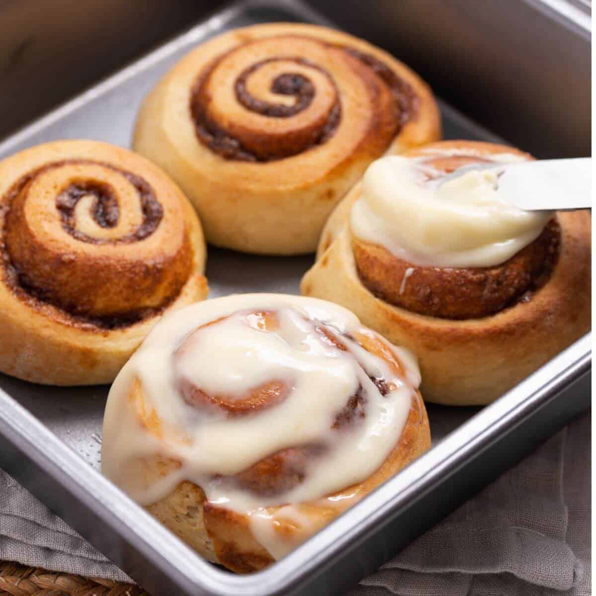 icing the baked cinnamon rolls in pan.