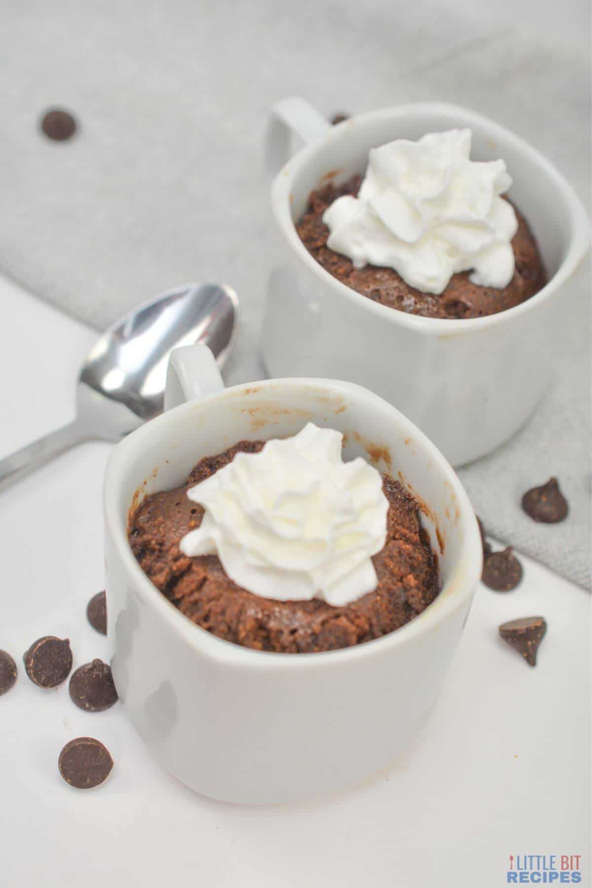 cakes in mugs topped with whipped cream.