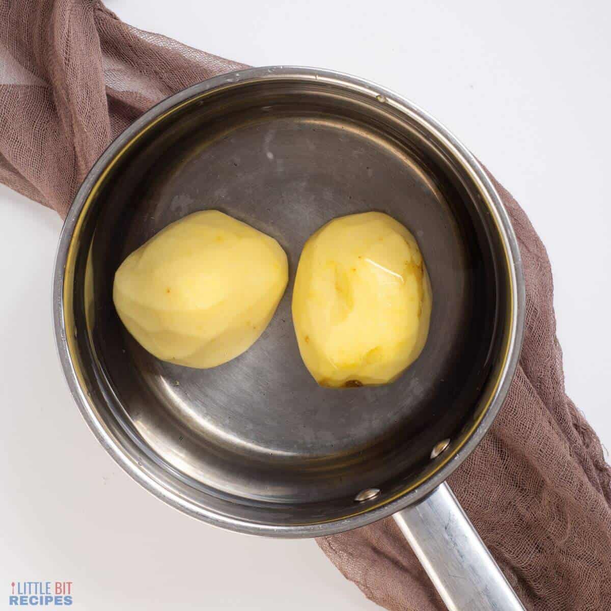 two peeled potatoes and water in saucepan.