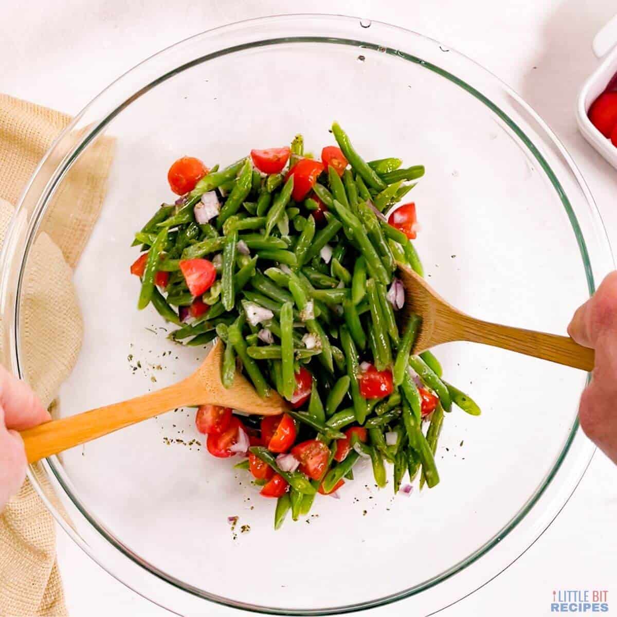 tossing the green bean tomato salad in glass mixing bowl.