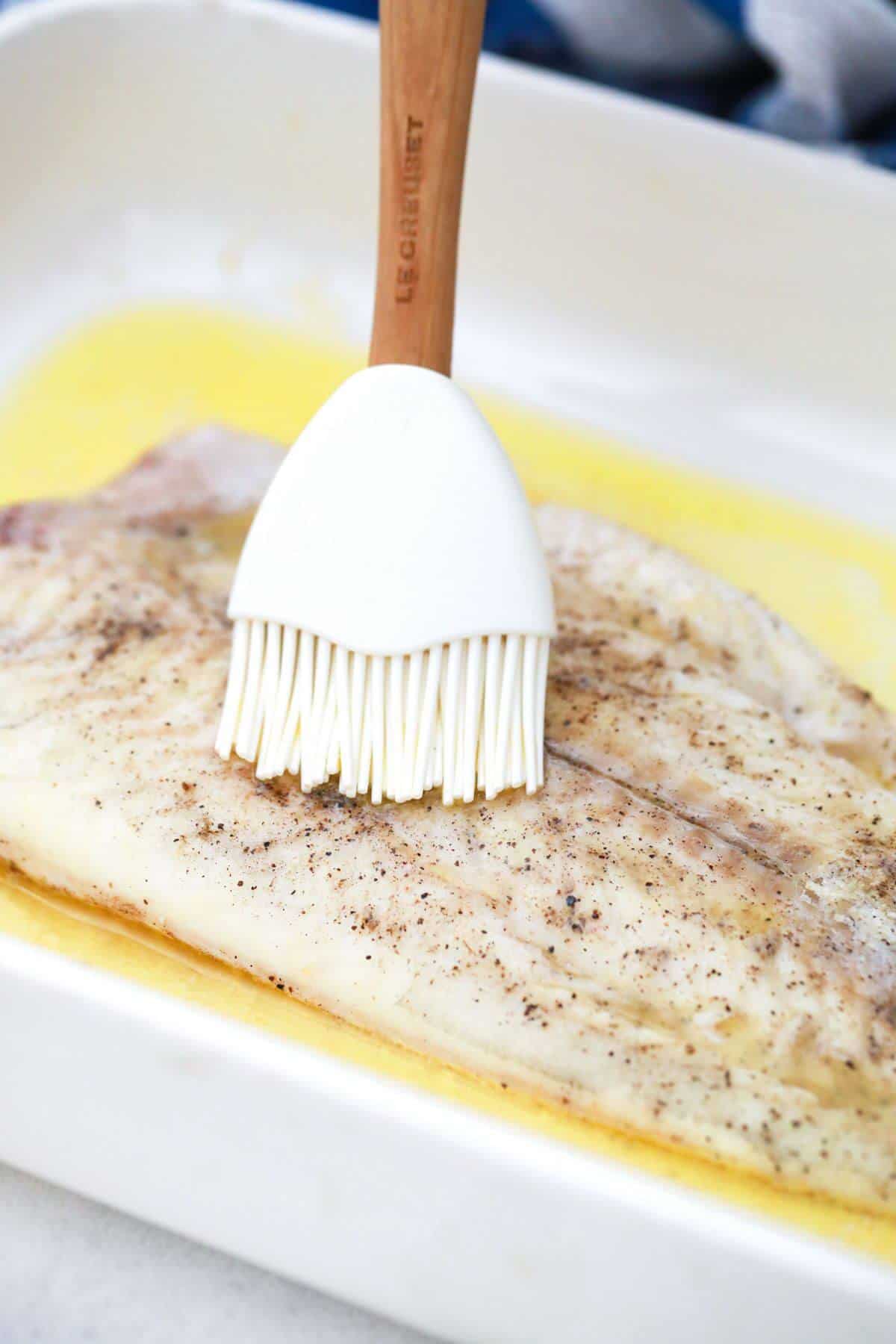 brushing seasoned fish fillet with butter.