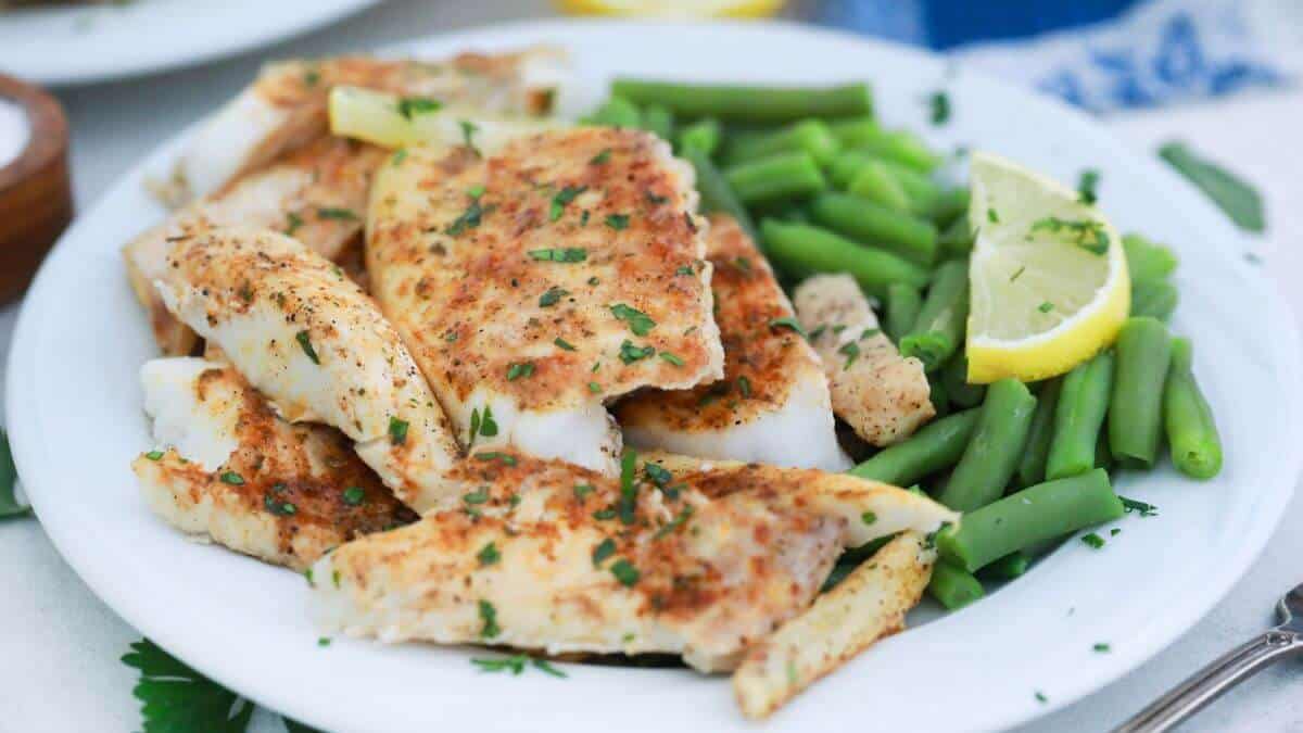 Baked butter fish on a plate with green beans.