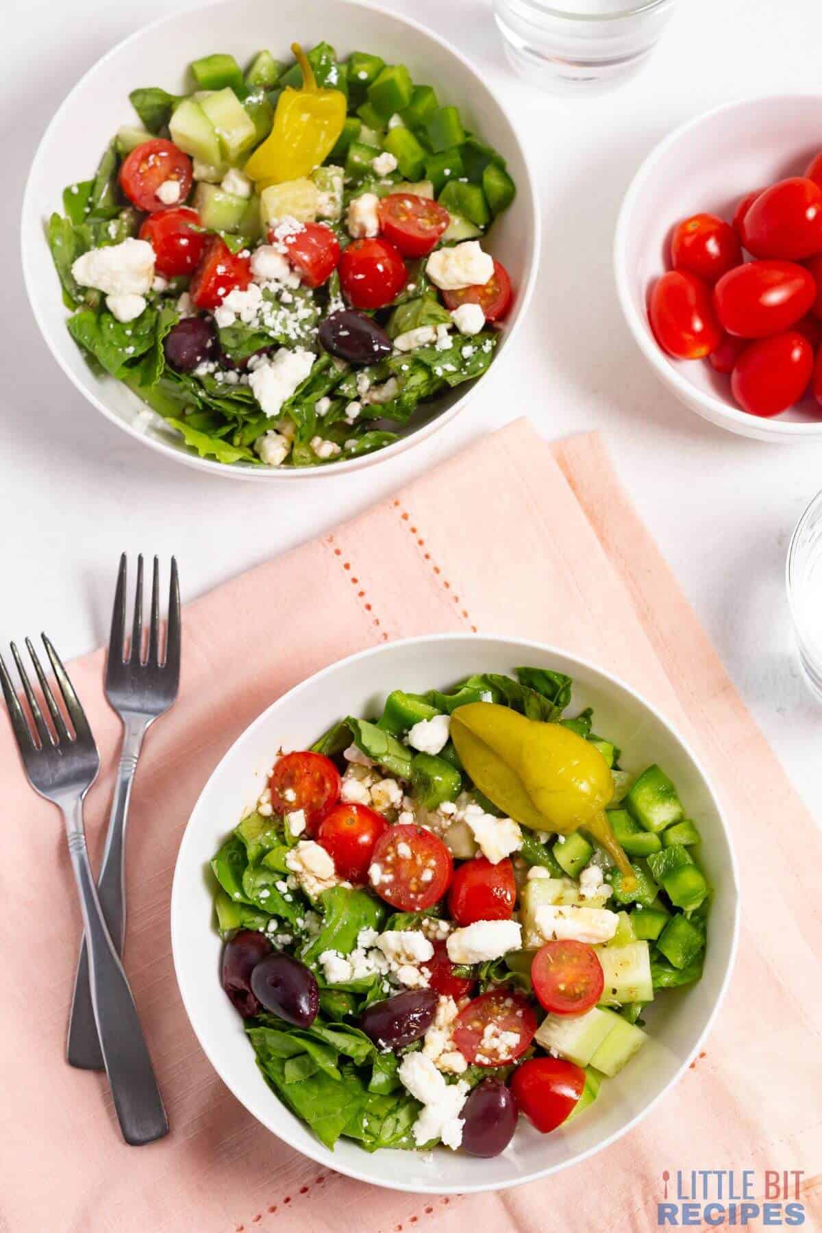 serving the chopped greek salad in two white bowls.