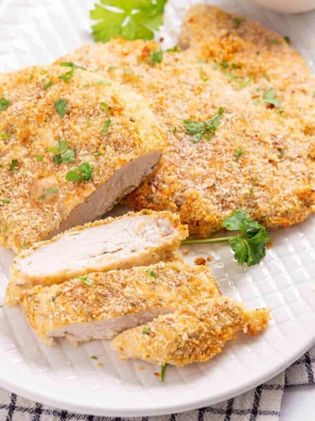 Breaded chicken breasts, partially sliced, garnished with parsley on a white plate.