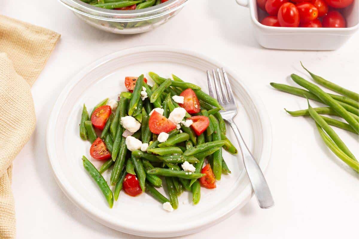 Green beans and tomatoes on a white plate.