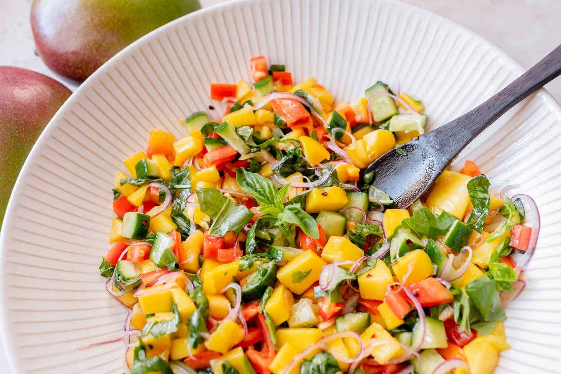 Mango salad with small wooden spoon on white plate.