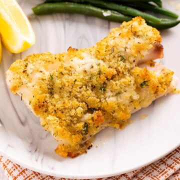 panko crusted cod fish on serving plate with green beans and lemon wedge.