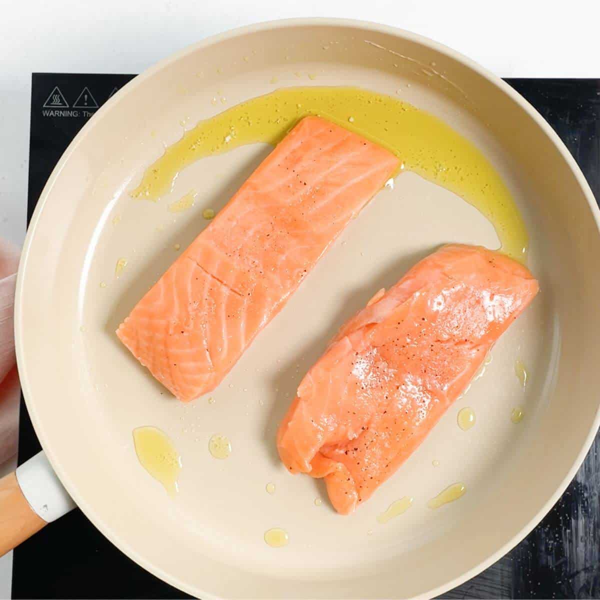 raw salmon fillets in frying pan with olive oil.