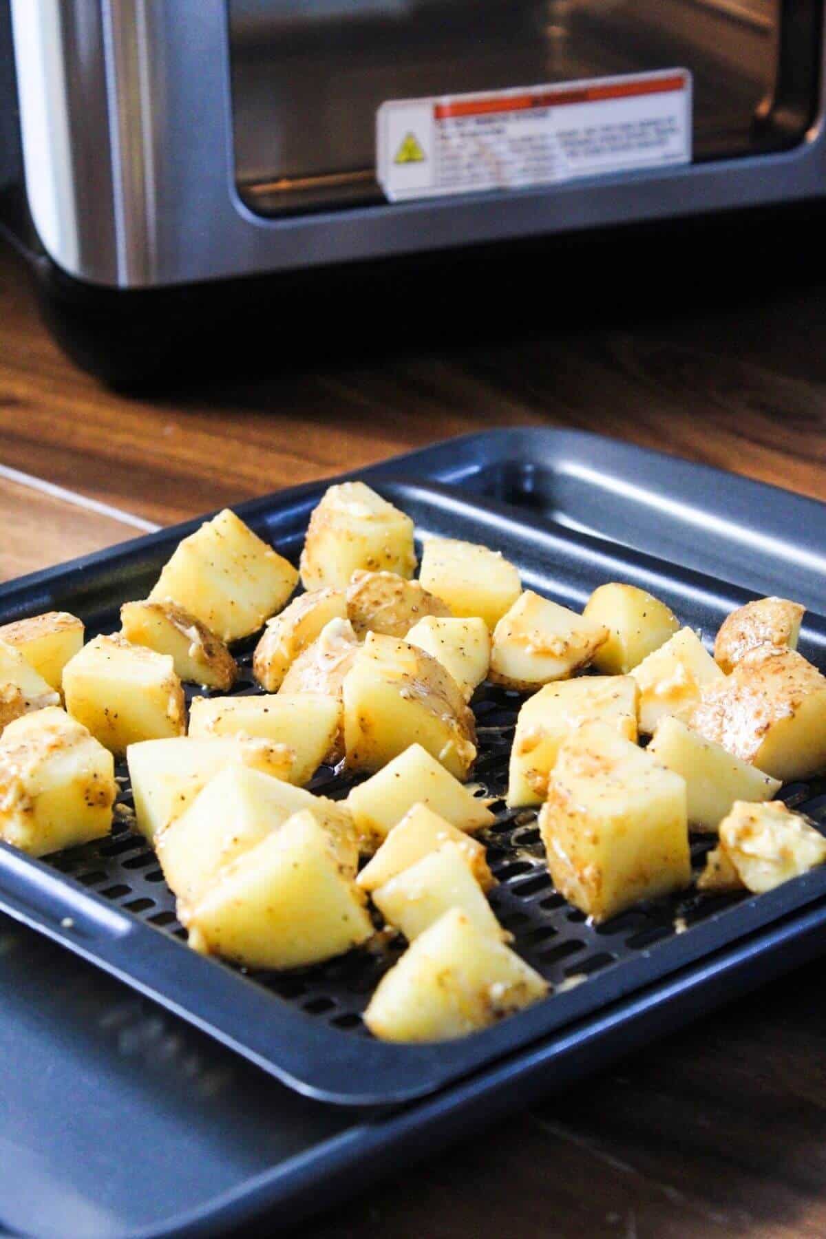Single layer of seasoned potatoes on air fryer tray.