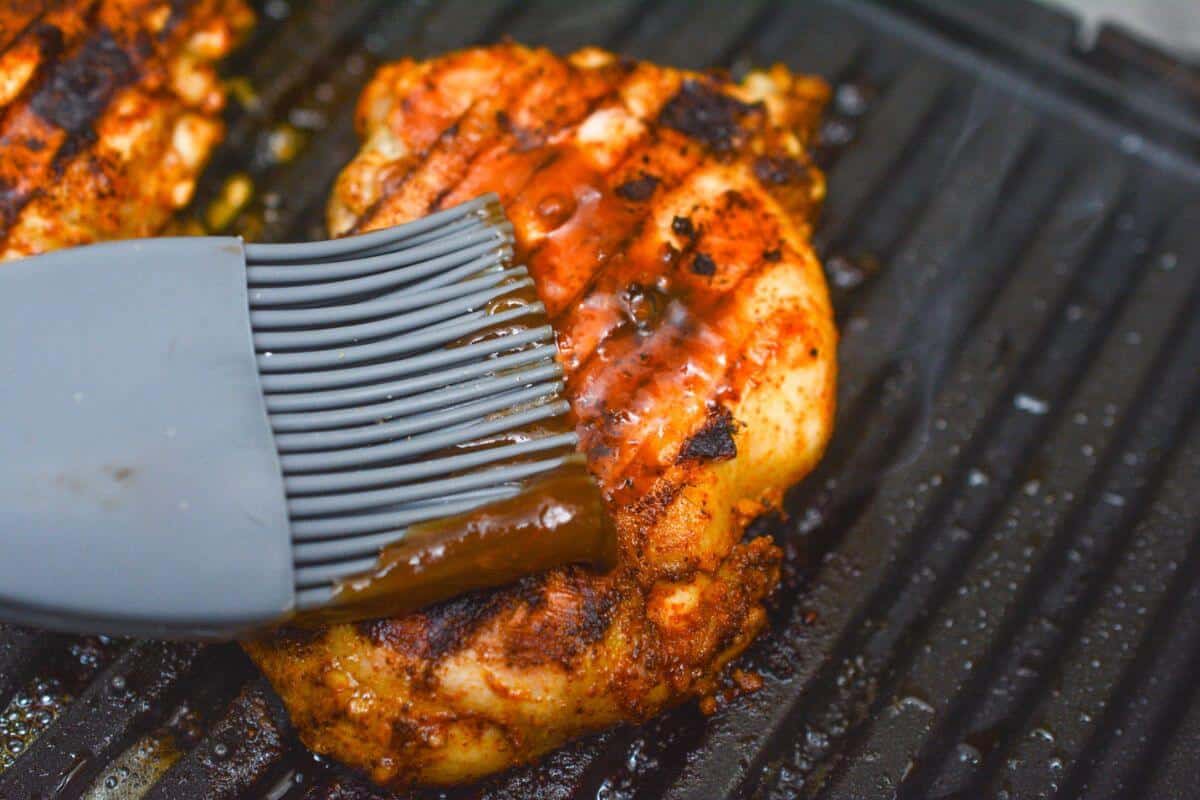 Brushing grilled boneless chicken thigh with bbq sauce.