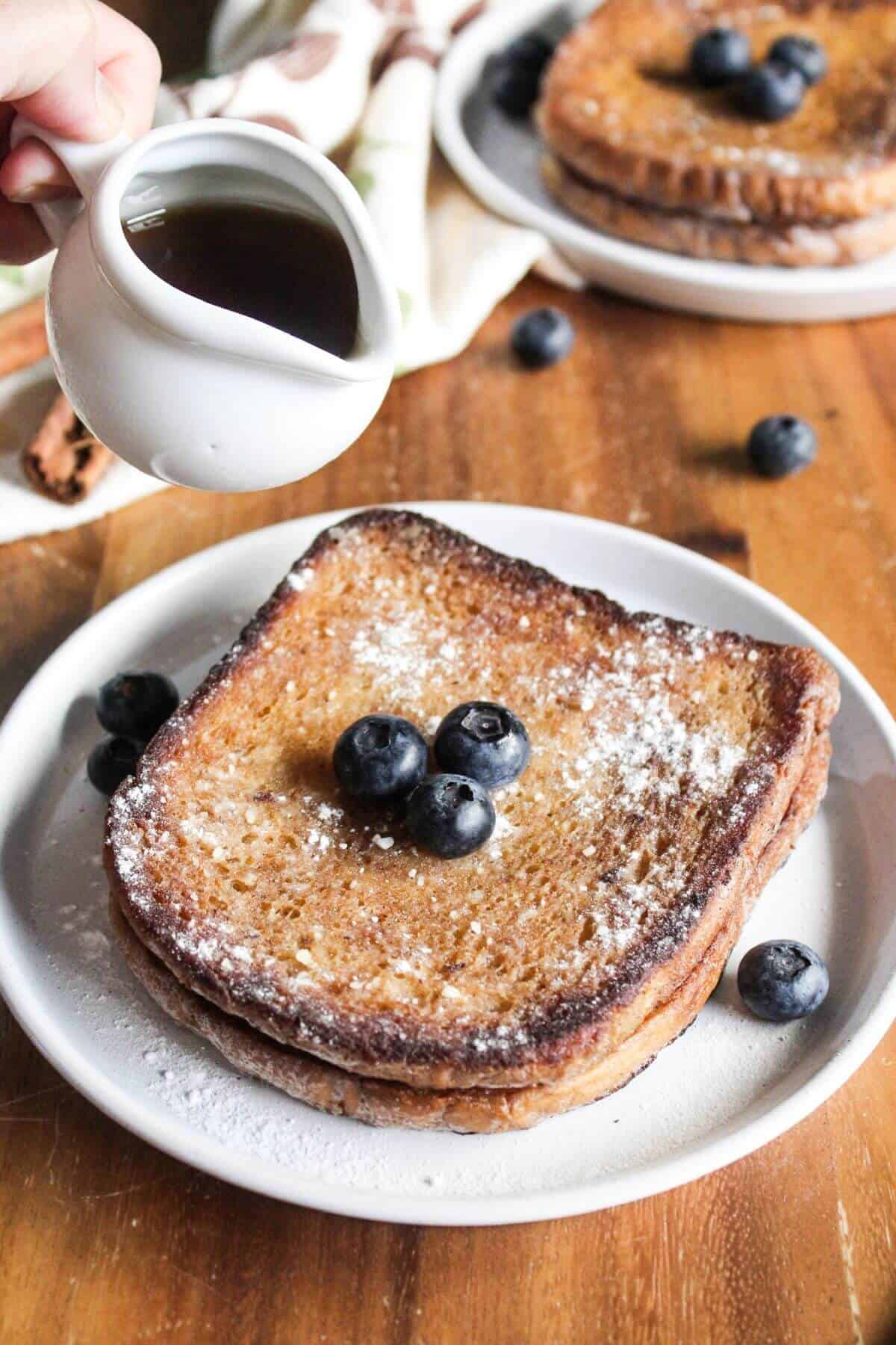 Pouring syrup over french toast with one.