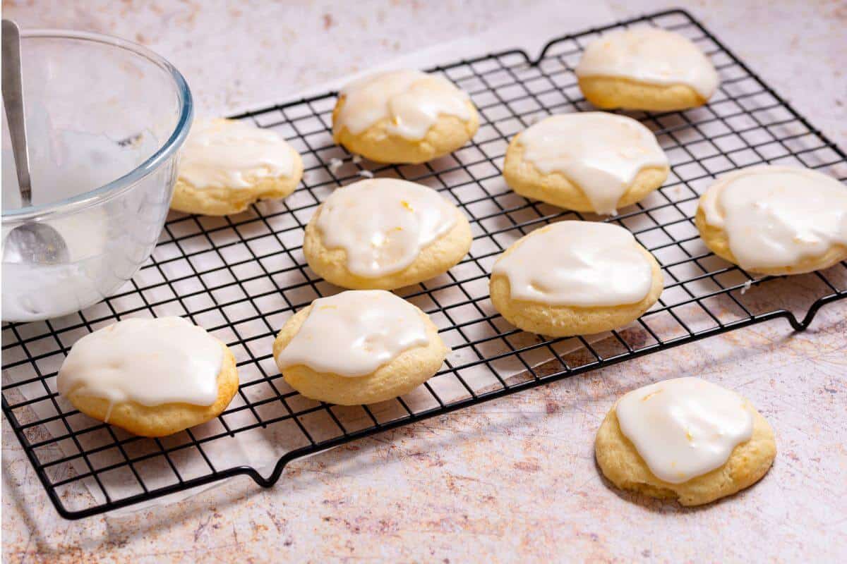 Lemon ricotta cookies on rack with icing bowl.