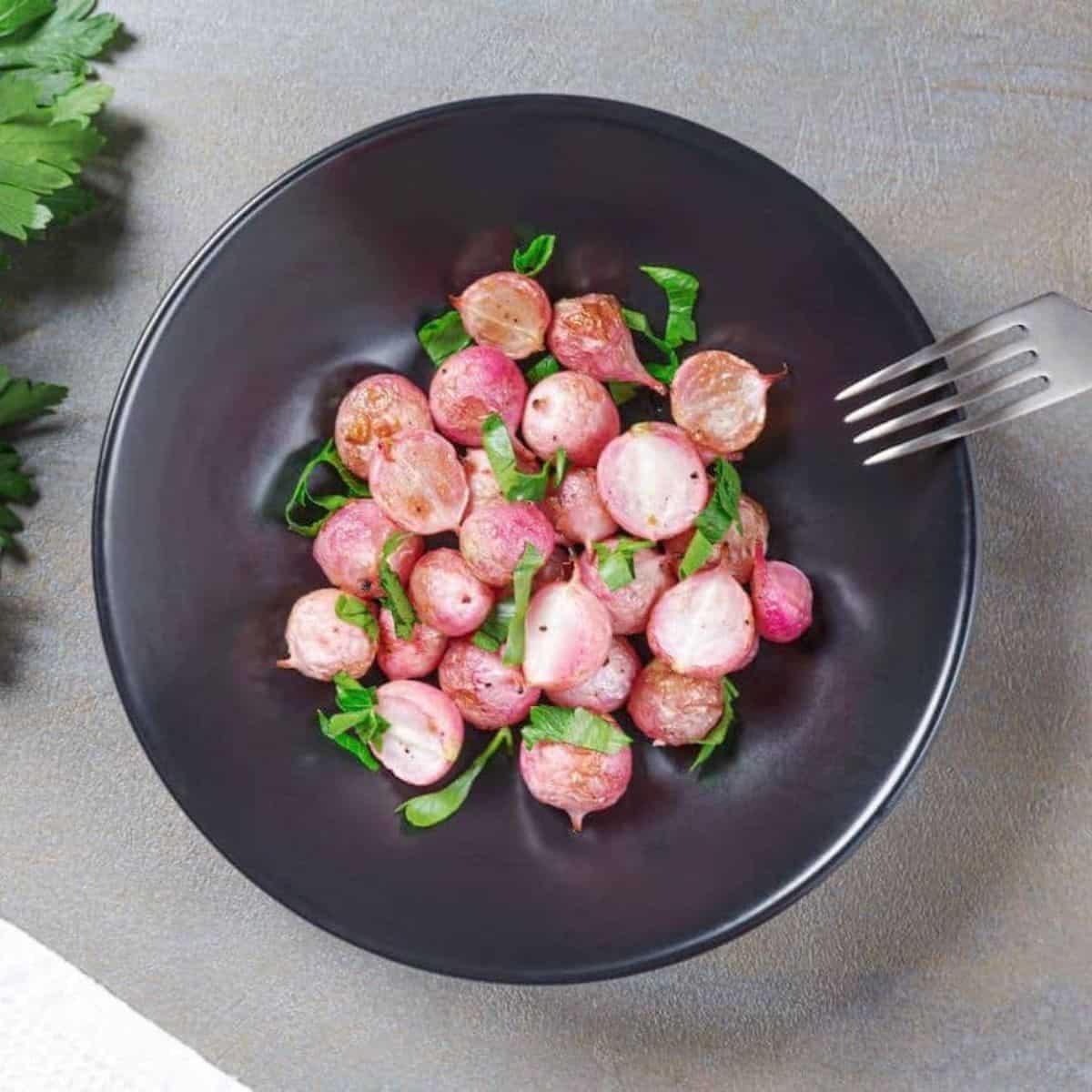Roasted radishes on a black plate.