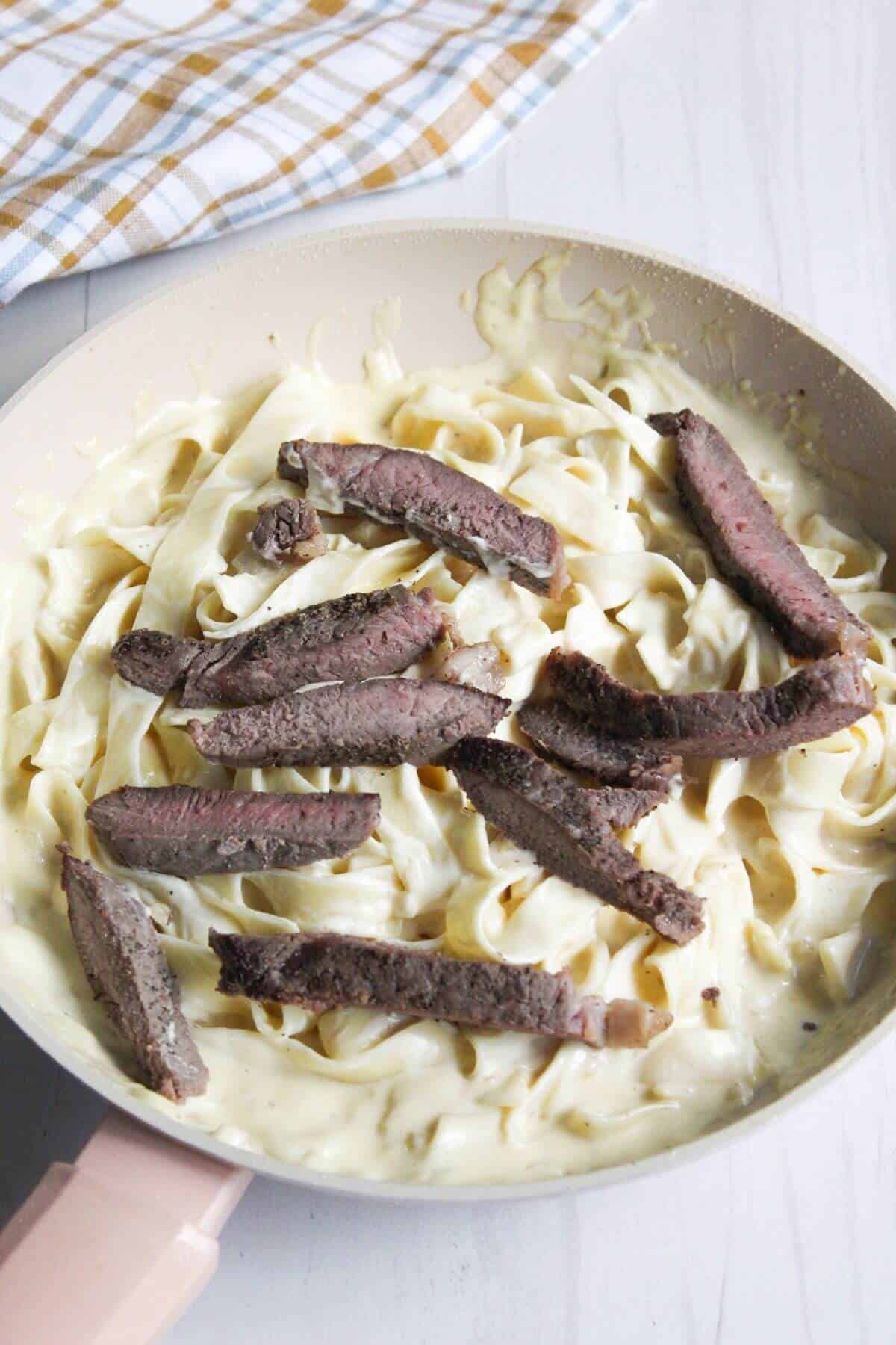 Steak added to pasta in skillet.