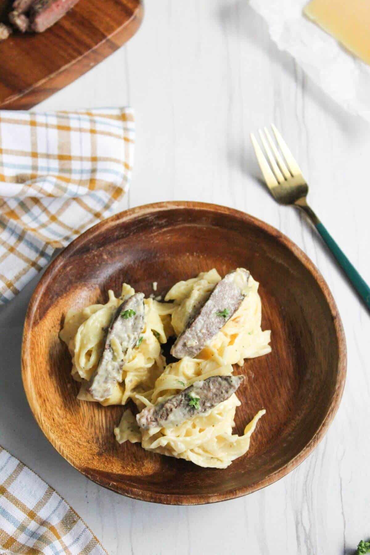 Wooden bowl with three pasta mounds topped with steak slice.