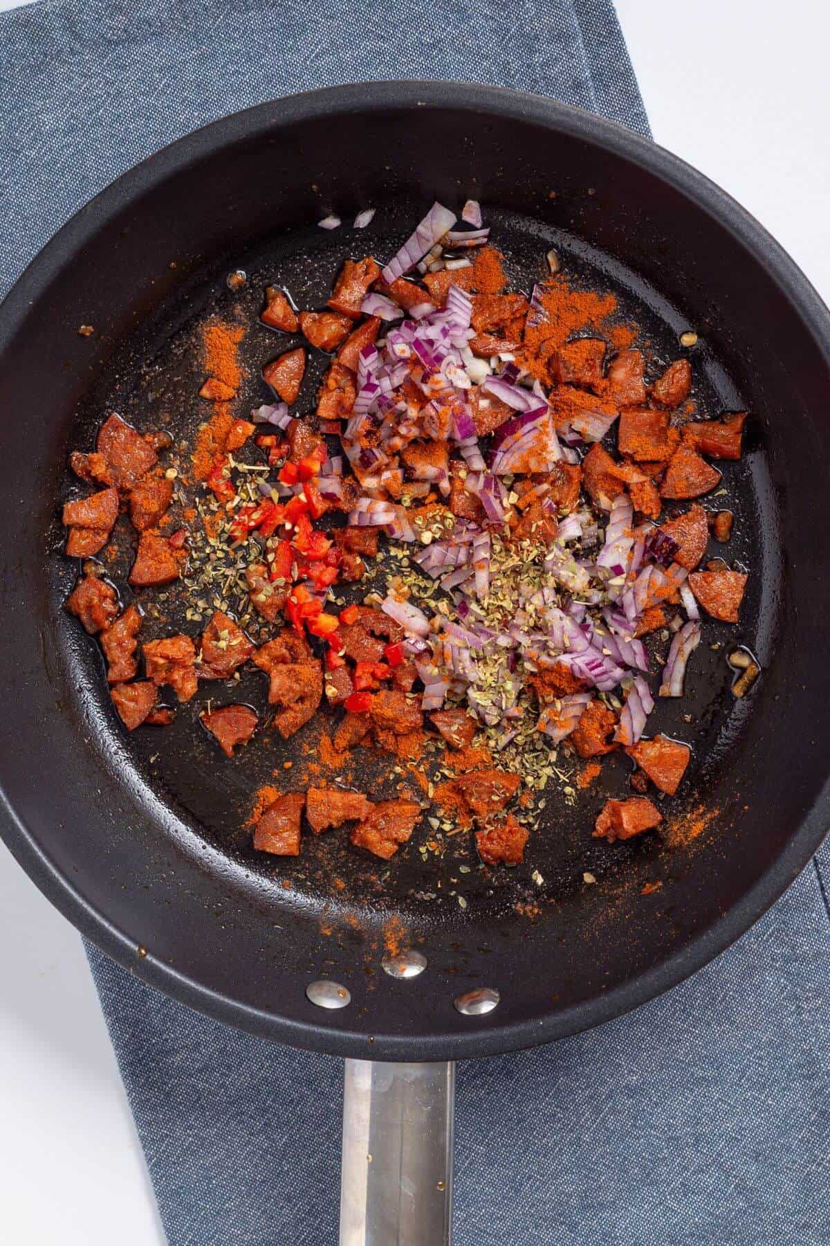 Onion and seasoning added to chorizo in skillet.