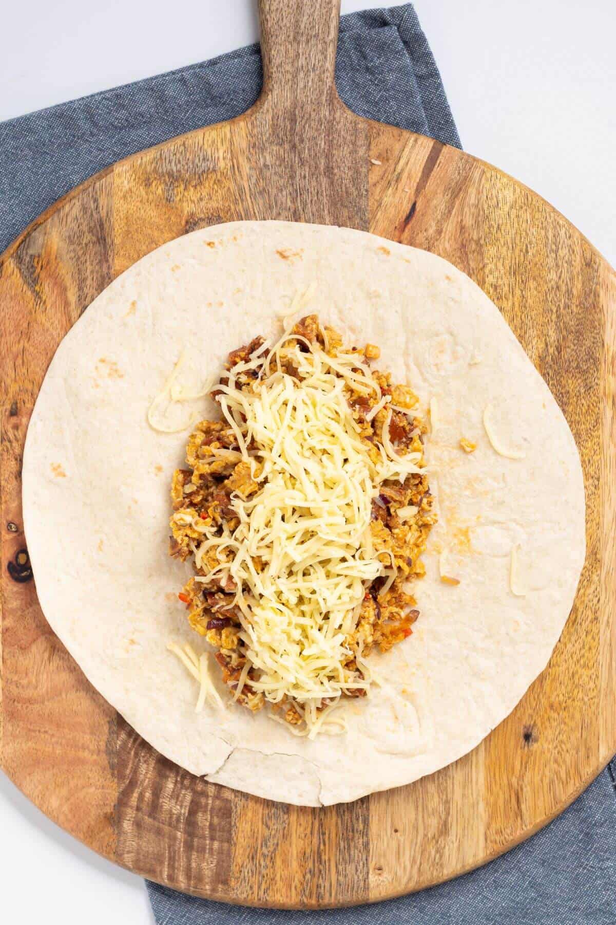 Assembling breakfast chorizo burrito on cutting board.