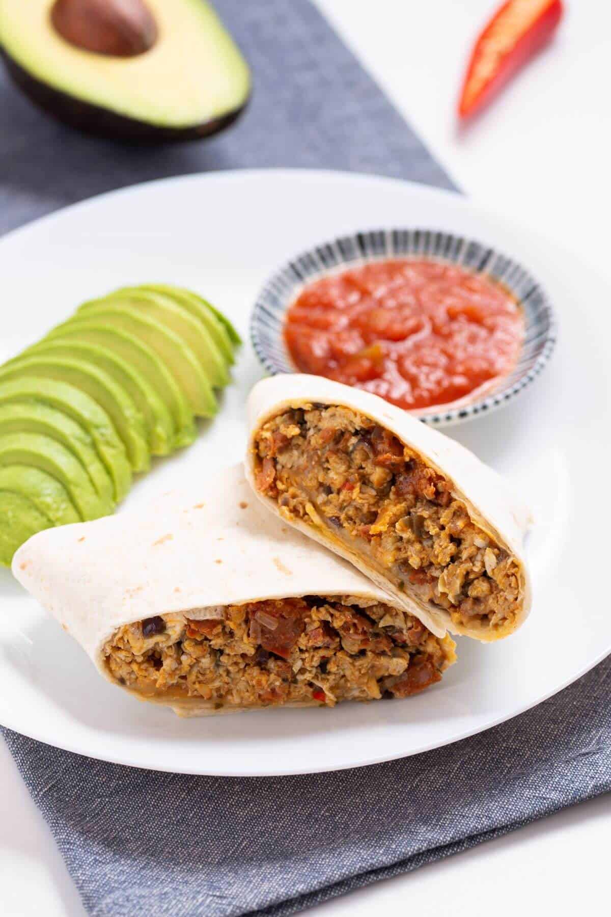 Breakfast chorizo burrito cut in half with avocado and salsa.