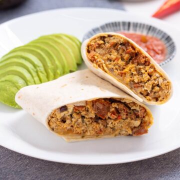 Breakfast burrito on plate with avocado slices and salsa.