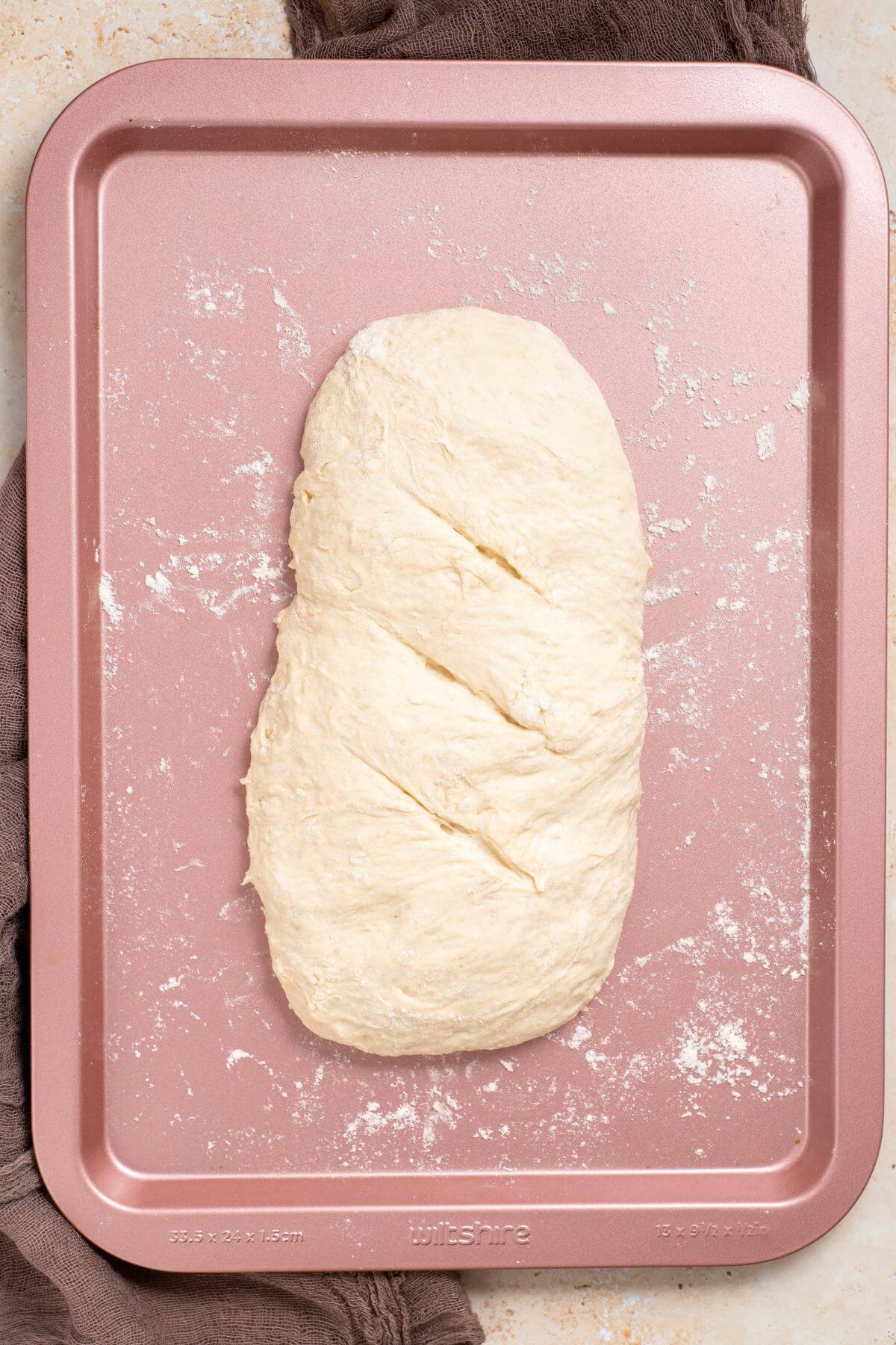 Risen dough shaped into loaf on floured baking sheet.