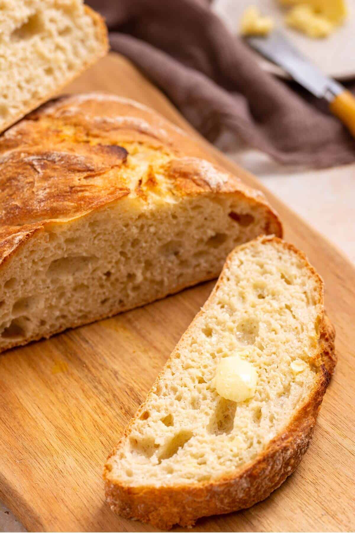 Sliced Italian artisan bread with buttered slice.