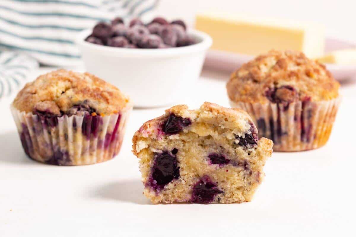 Three blueberry muffins with front one cut in half.