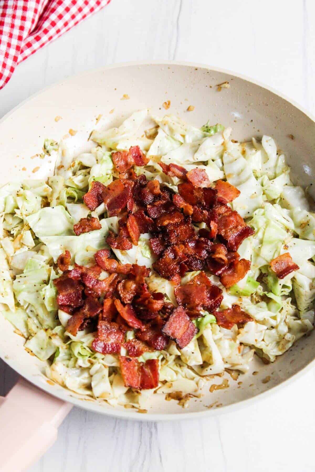 Cooked bacon pieces added to cabbage in skillet.