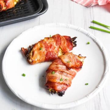 Two bacon wrapped cabbage wedge on white plate.