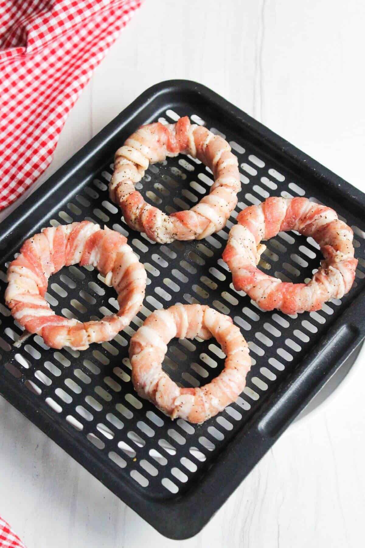 Bacon wrapped onion rings on air fryer tray.