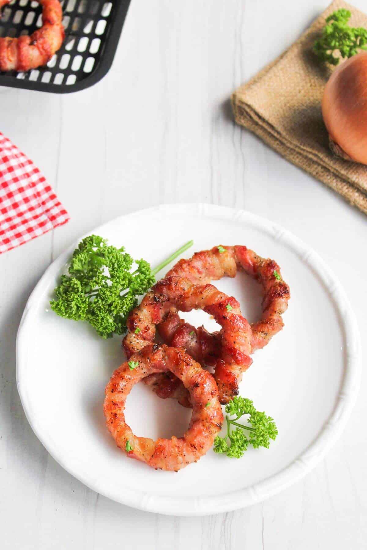 Bacon wrapped onion rings on white plate.