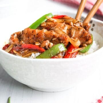 Black pepper chicken with chopsticks and rice in bowl.