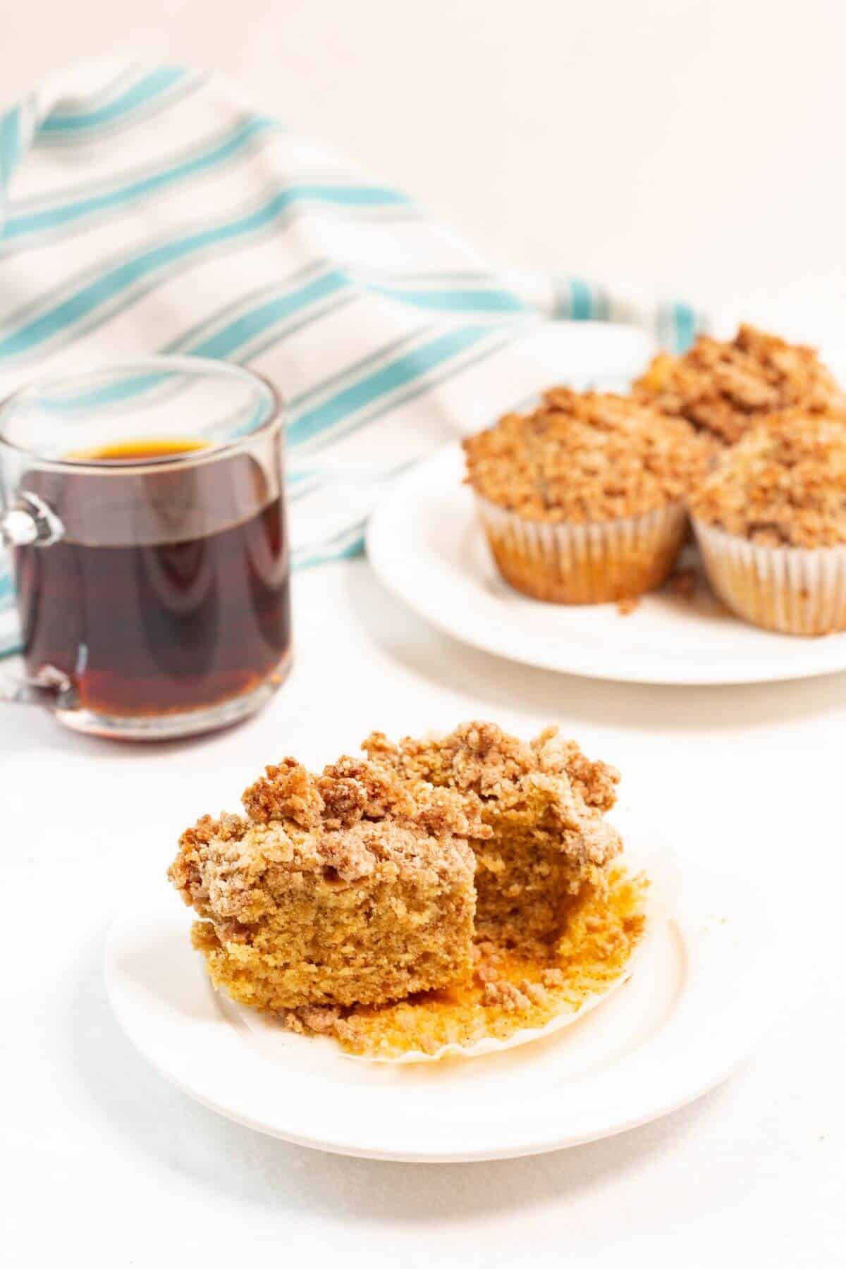 Coffee cake muffin sliced in half on plate with coffee.