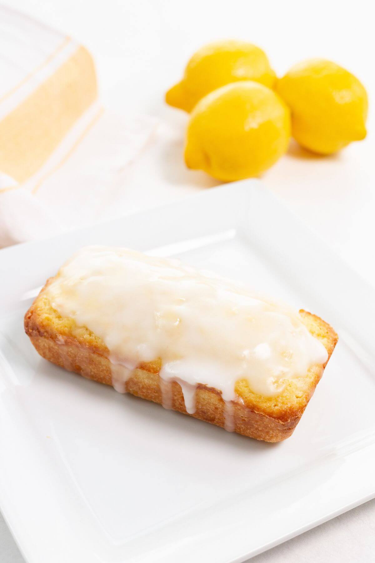 Glazed lemon loaf on square white plate.