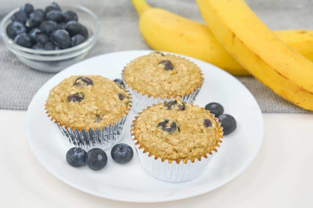 Three oat blueberry muffins on a white plate.