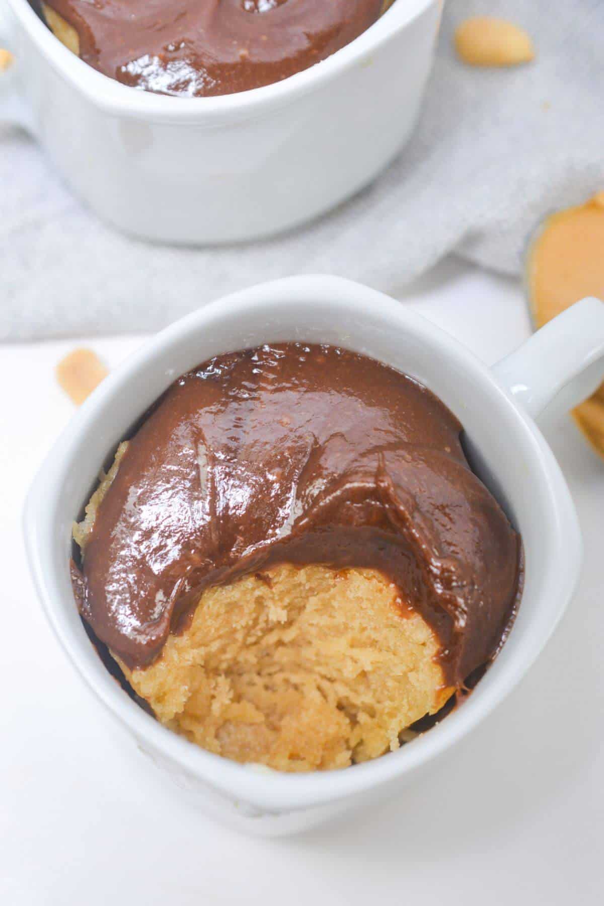 Chocolate frosted peanut butter mug cake with bite missing.