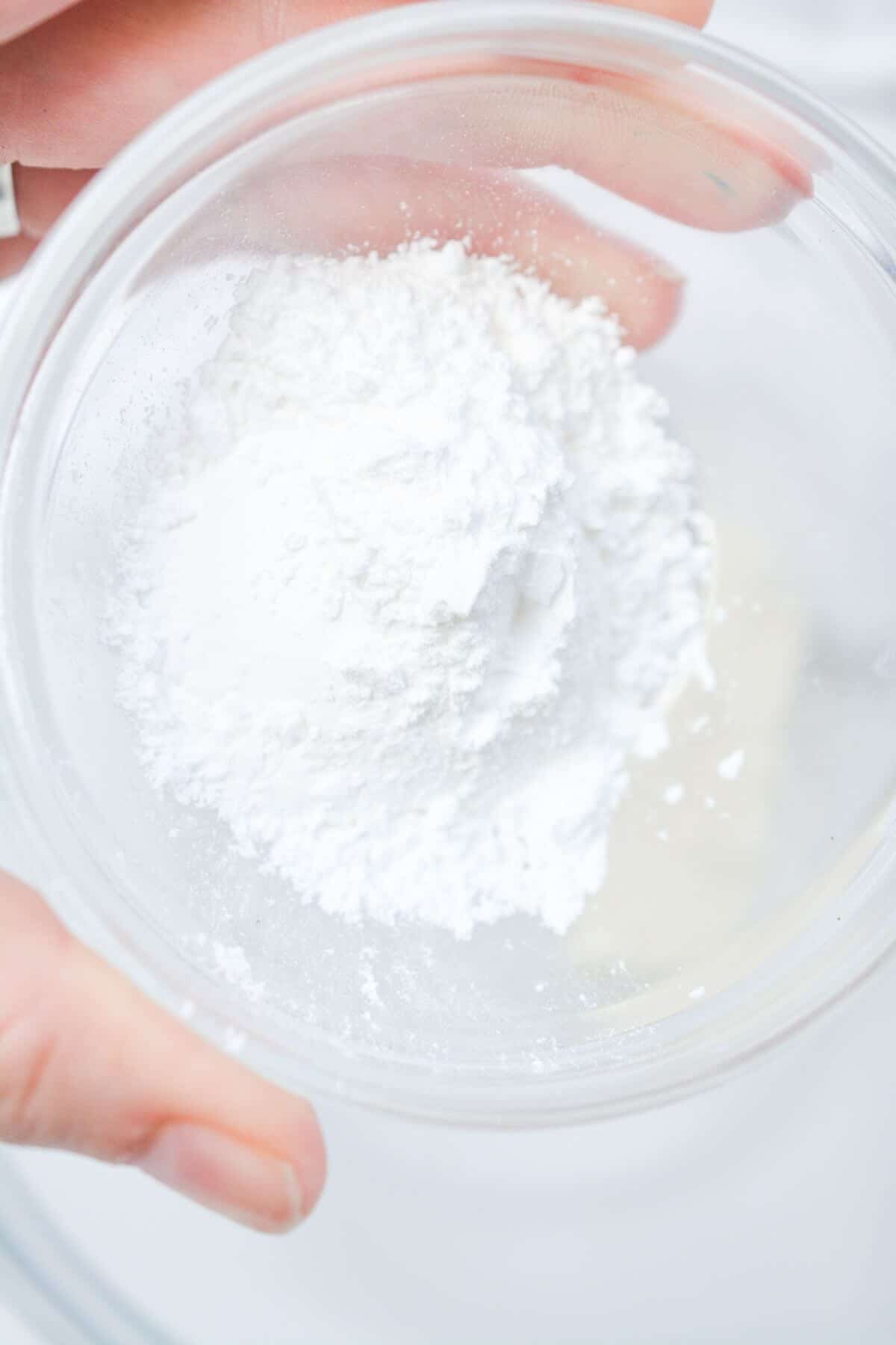 Adding sugar to cream cheese in mixing bowl.