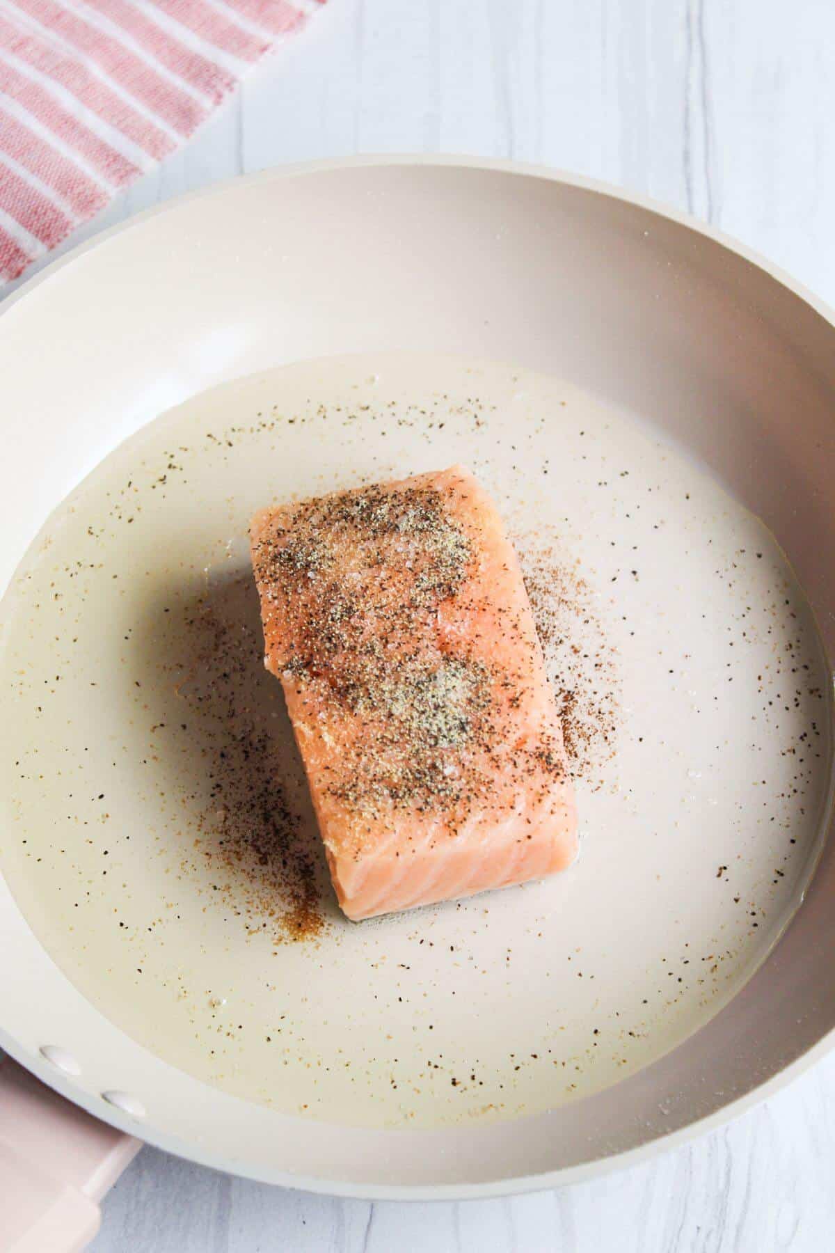 Seasoned salmon fillet in hot skillet.